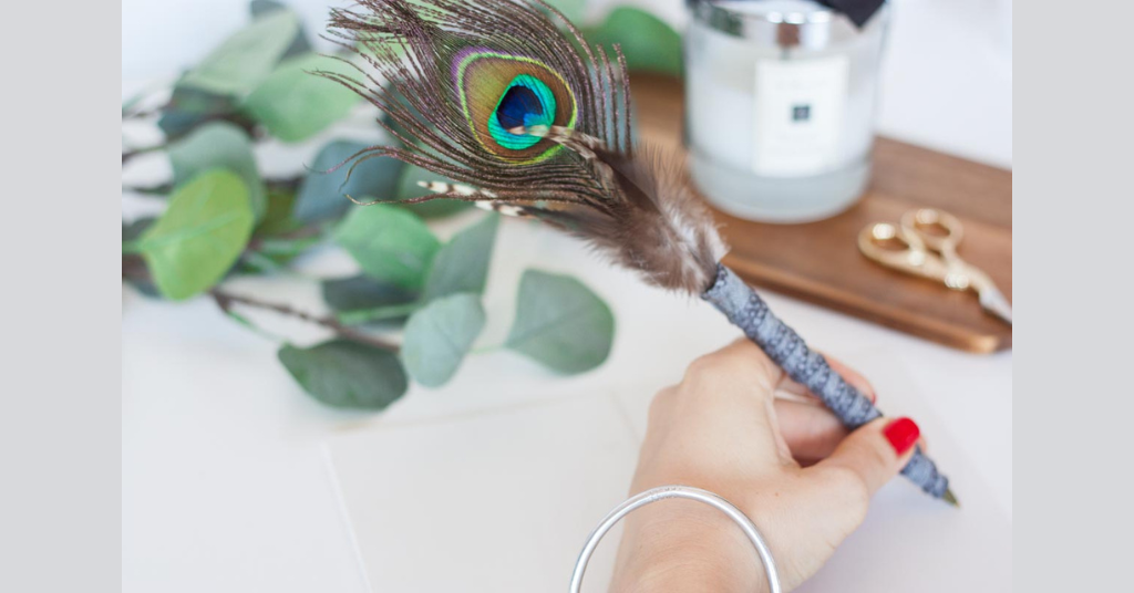 A person is holding handmade pen with peacock feather